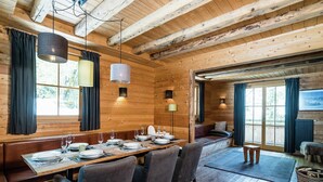 A wooden interior with a dining table set for six, benches, and a seating area with cushions.