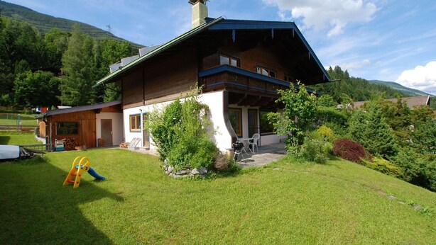 A two-story chalet with a sloped roof, a wooden exterior, and a stone foundation. There is a small patio with outdoor seating and a children's playset. - Chalet in Neukirchen near Ski Lifts (Neukirchen am Großvenediger)
