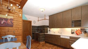 A kitchen with wooden cabinets, a tiled floor, and a dining area with a chair and table. - Chalet in Neukirchen near Ski Lifts (Neukirchen am Großvenediger)