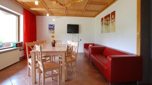A dining area with a wooden table and chairs, a red sofa, and a television on the wall. - Chalet in Neukirchen near Ski Lifts (Neukirchen am Großvenediger)