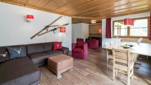 Uma sala de estar moderna com teto de madeira, um sof á seccional marrom, cadeiras vermelhas e marrons, uma mesa de jantar de madeira e uma lareira.
