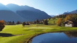 Um campo de golfe tranquilo com lago, casas e montanhas ao fundo.