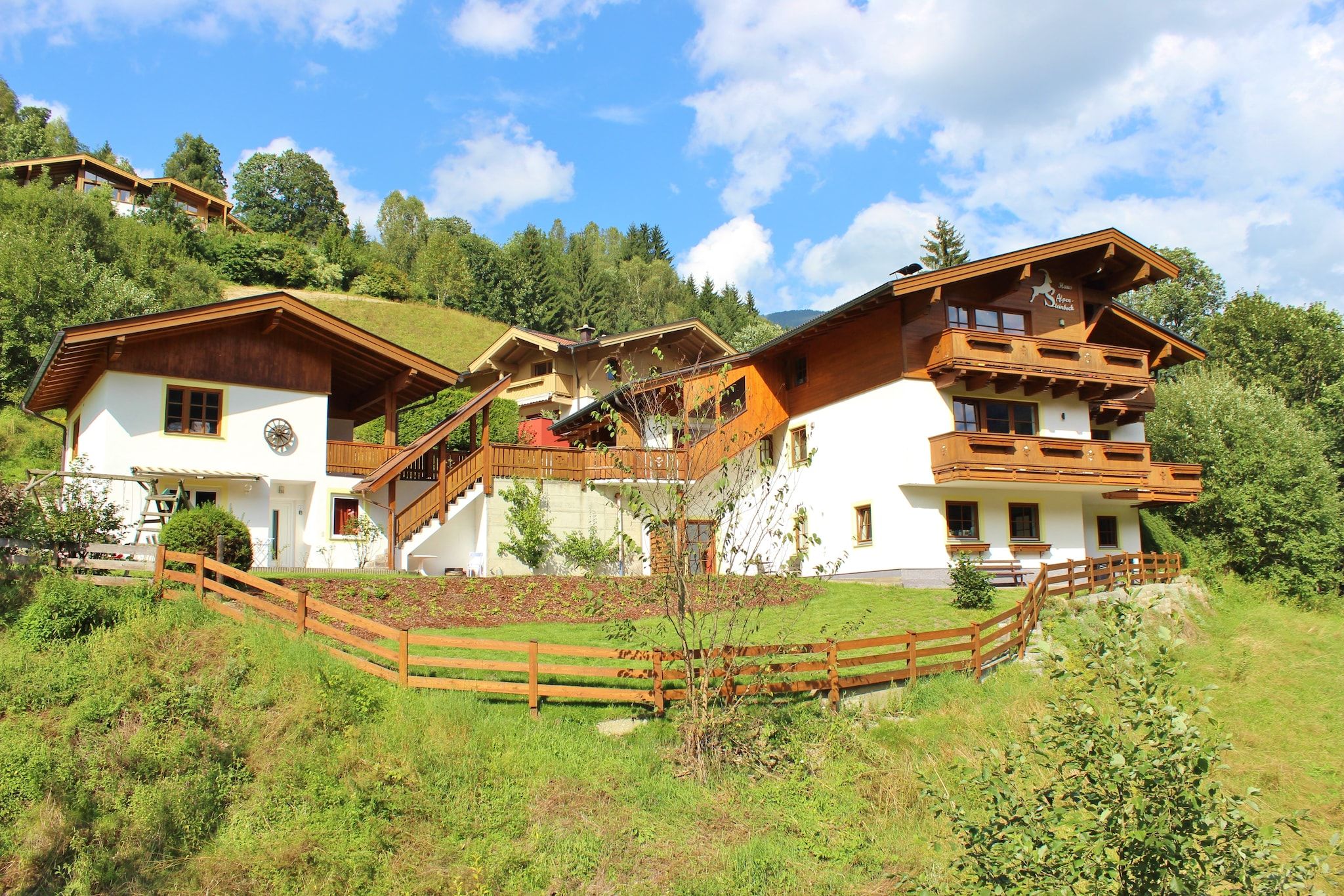 A large, multi-story chalet with a wooden exterior, set on a hillside with a wooden fence in the foreground.