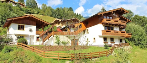 Ein großes, mehrstöckiges Chalet mit Holzfassade, gelegen an einem Hang, im Vordergrund ein Holzzaun.