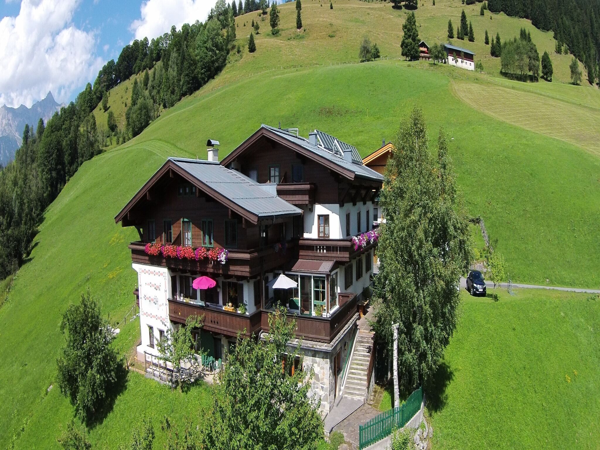 Een chalet met twee verdiepingen en een balkon, omringd door weelderige groene heuvels en een berg op de achtergrond.