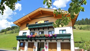 A two-story building with a wooden facade, large windows, and a balcony with colorful flower boxes. - Chalet in Maria Alm near Hochkönig Ski Lift (Maria Alm)