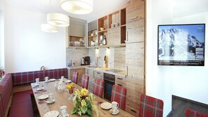 A modern kitchen with wooden cabinetry, a dining area with plaid upholstered benches, and a large flat-screen TV mounted on the wall. - Chalet in Maria Alm near Hochkönig Ski Lift (Maria Alm)