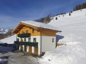 Eine Holzhütte mit geneigtem Dach, umgeben von verschneiter Landschaft und klarem Himmel.