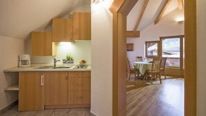 A compact kitchen with wooden cabinets, a sink, and a coffee maker. There is a dining area with a table and chairs, and a view of the outside through large windows. - Apartment in Kaltenbach near Ski Lift (Kaltenbach)