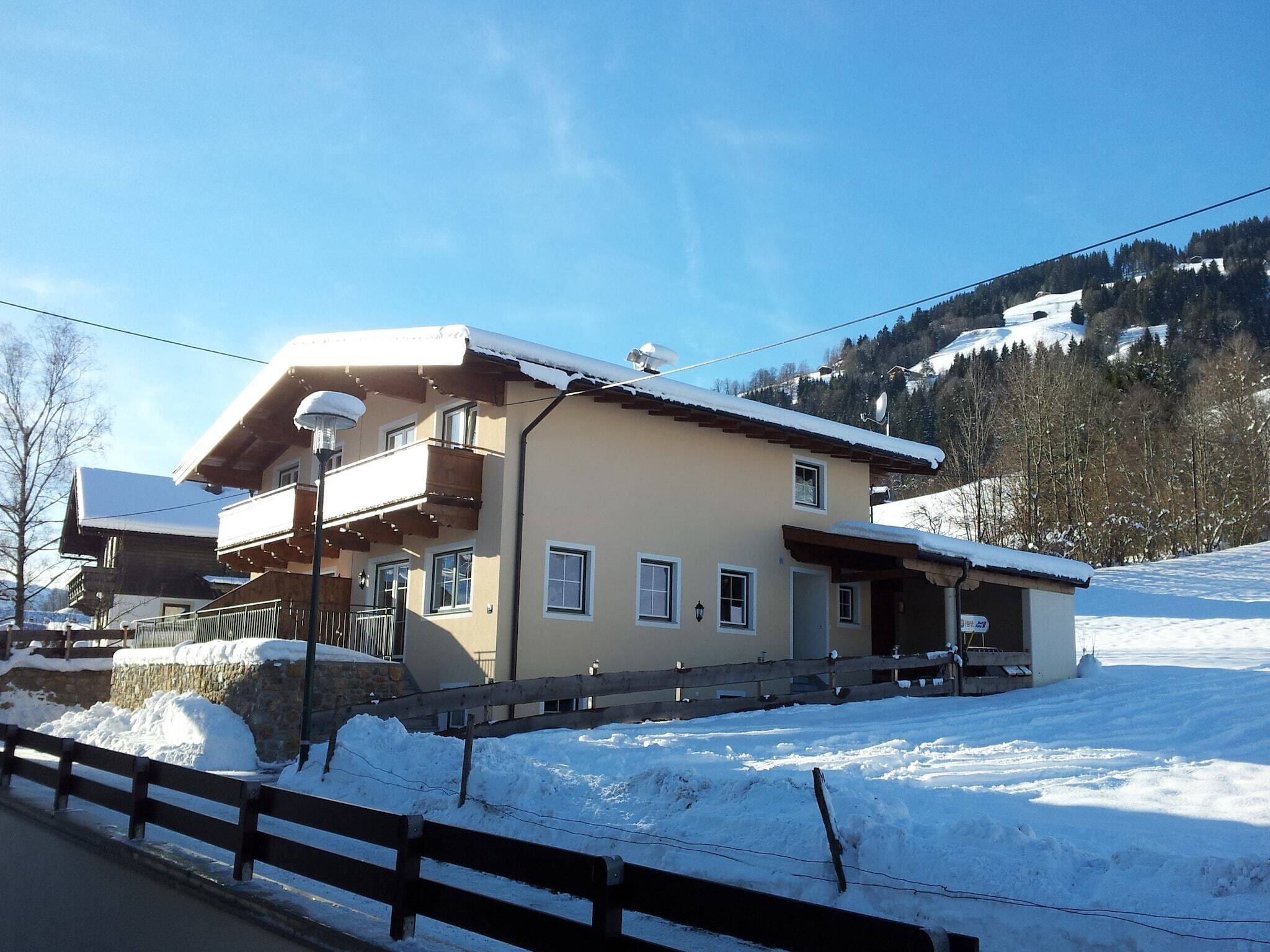 Ein zweistöckiges Chalet mit Balkon, ein Skilift im Hintergrund und eine verschneite Landschaft.