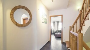 A hallway with a wooden-framed mirror, a staircase with wooden railings, and a view into a living room with a sofa and curtains. - Holiday Home Brixen near Skiwelt Slopes (Brixen im Thale)