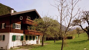 Una casa de madera con balcón, rodeada de césped y árboles.
