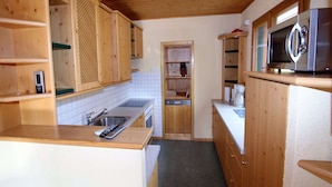 Een kleine keuken met houten kastjes, een roestvrijstalen spoelbak, een magnetron en een vaatwasser.