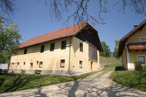 A two-story building with a red-tiled roof, a stone foundation, and a grassy area in front.