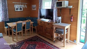 Ein gemütliches Zimmer mit Holzeinrichtung, einem Fernseher, einer Kaffeemaschine und einem Essbereich mit Stühlen und einem Tisch.