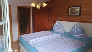 Ein Schlafzimmer mit Bett, Holz-Kopfstück, einer Chandelüster, einem gerahmten Bild an der Wand und einer Tür.