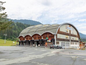 A large, modern building with a curved roof, labeled 'Millennium-Express'. It features multiple ticket counters, a luggage area, and a parking lot with several cars. - Apartment in Tröpolach near Nassfeld (Tröpolach)