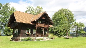 A wooden house with a sloped roof, a balcony, and a stone foundation.