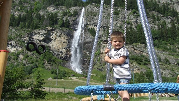 A child playing on a swing set with a waterfall in the background.