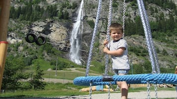 A child playing on a swing set with a waterfall in the background.