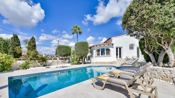 A swimming pool with lounge chairs, surrounded by a white building and trees.