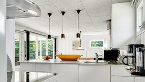 A modern kitchen with white cabinets, a large stove, a sink, and a coffee maker.