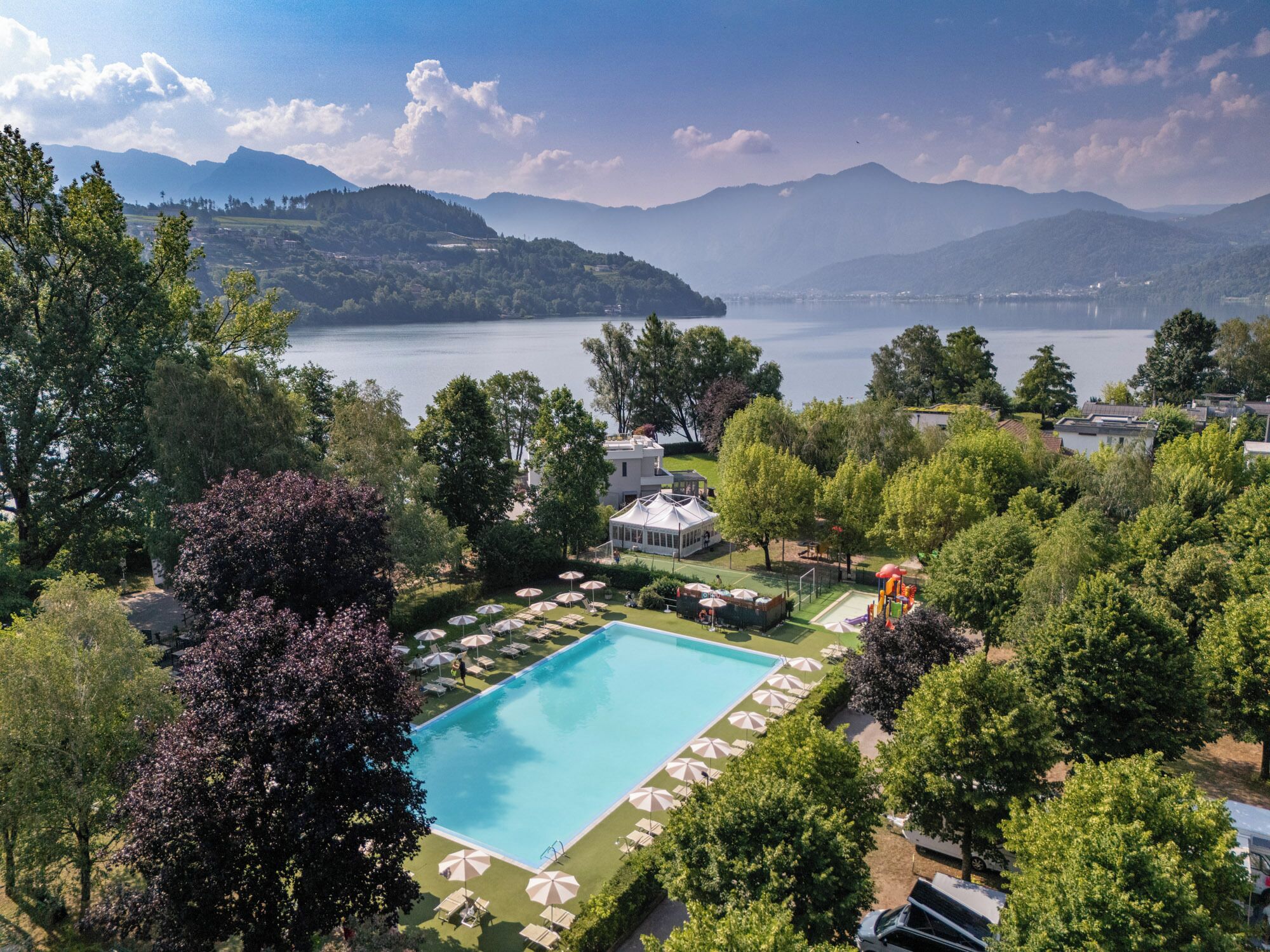 Una piscina immersa nel verde, con vista su un lago e montagne sullo sfondo.