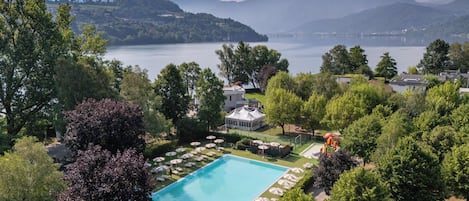 Una piscina rodeada de exuberante vegetación, con vista a un lago y montañas al fondo.