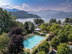 A swimming pool surrounded by lush greenery, with a view of a lake and mountains in the background. - Club del Sole Caldonazzo Family Collection (San Cristoforo)