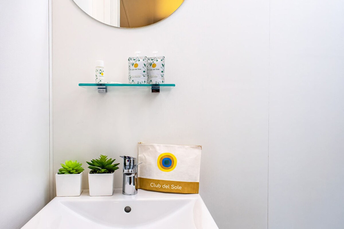 A bathroom with a white sink, two potted plants, a mirror, and a shelf with toiletry items.