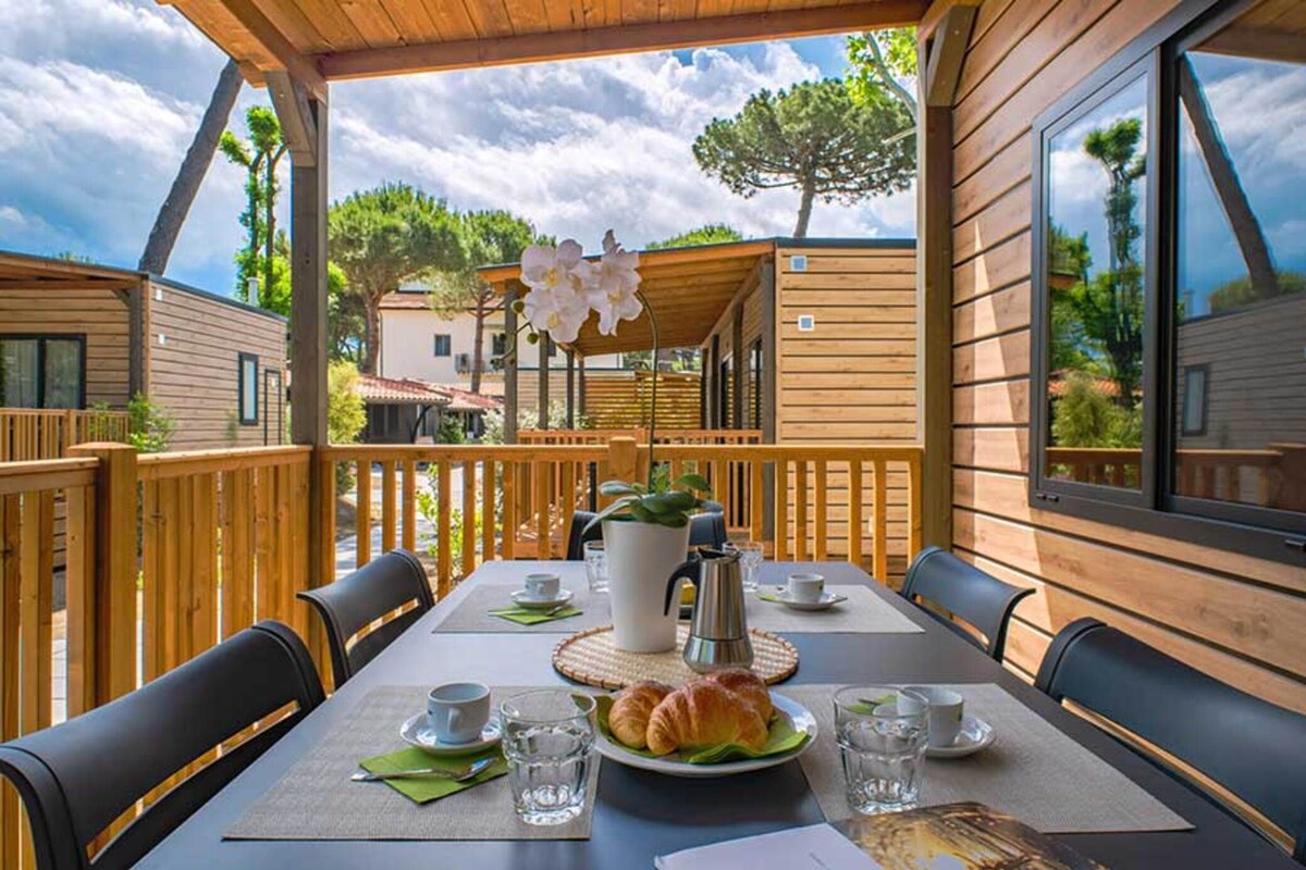 A wooden deck with a table set for breakfast, including croissants and coffee.