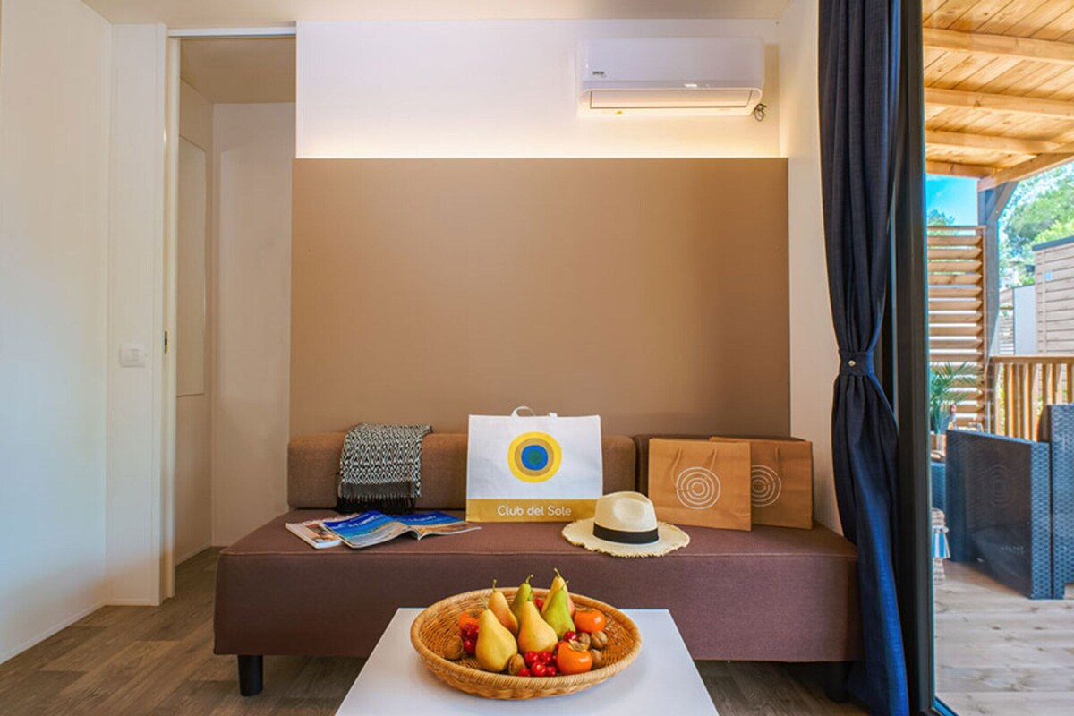 A cozy room with a brown sofa, a wicker fruit basket, a white bag, and a hat on the sofa.