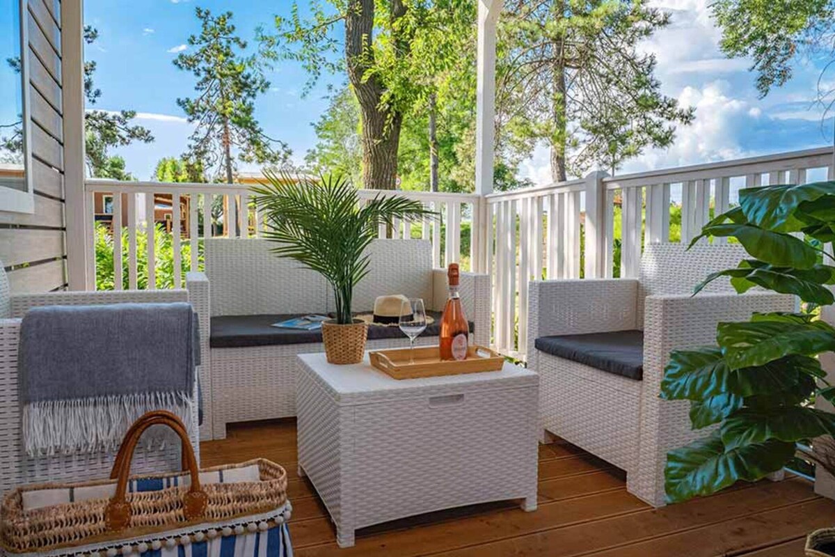A covered outdoor seating area with wicker furniture, a table with a bottle and glass, and a basket.