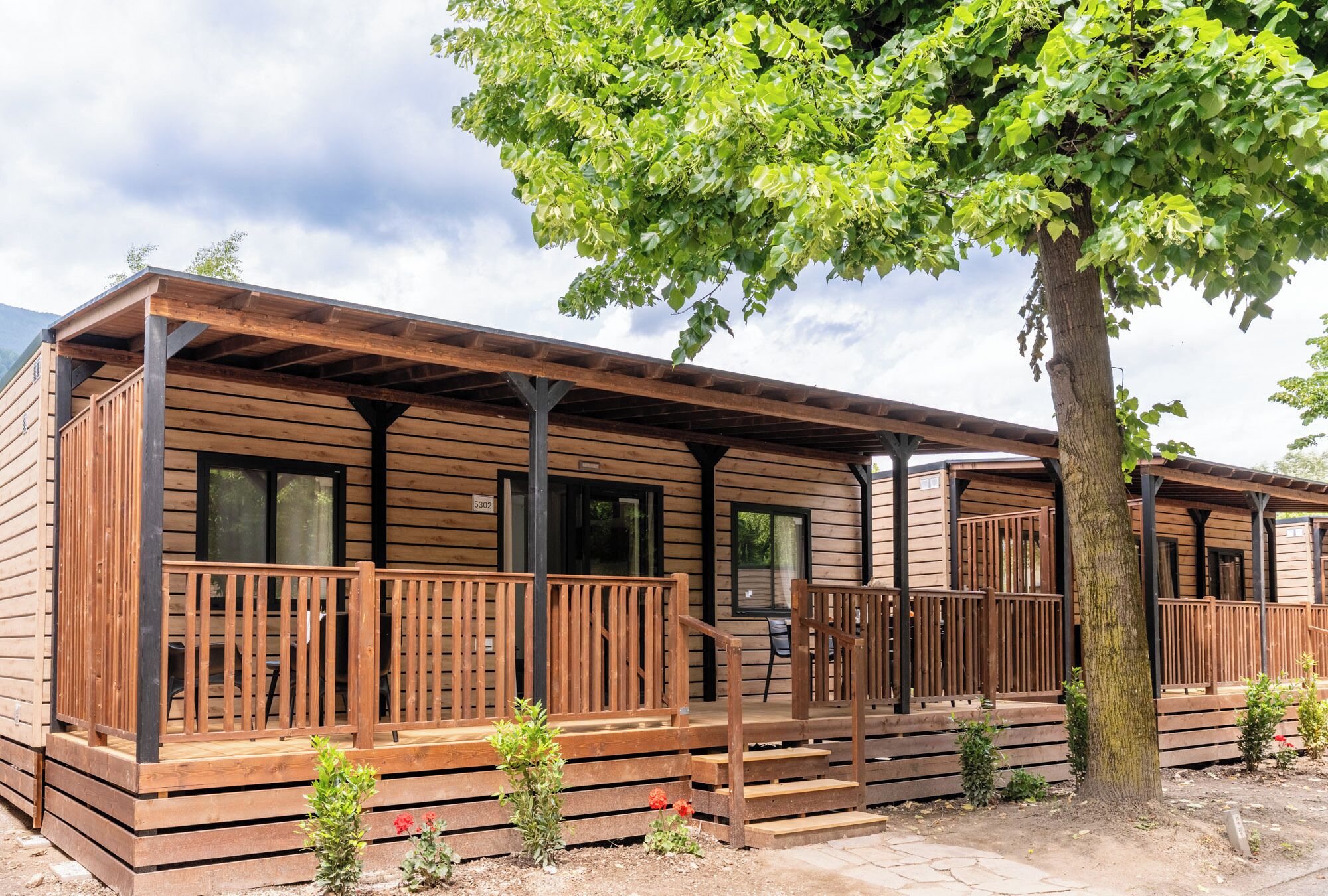 A wooden cabin with a porch, a small garden, and a tree.