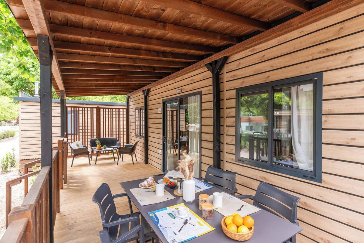 A covered outdoor dining area with wooden walls, a table with chairs, and a view through large windows.