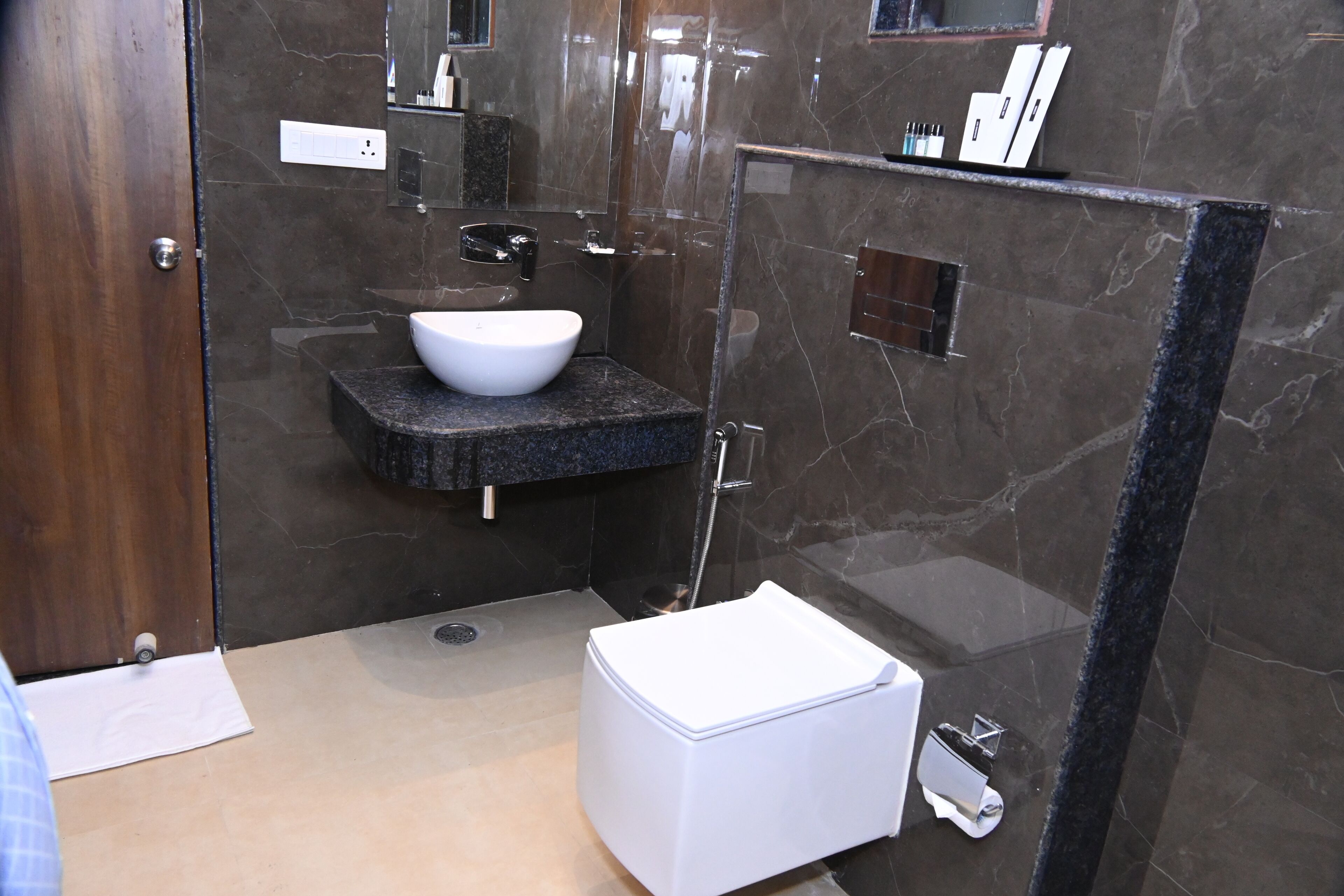 A modern bathroom with a white sink, dark marble walls, and a glass shower enclosure.