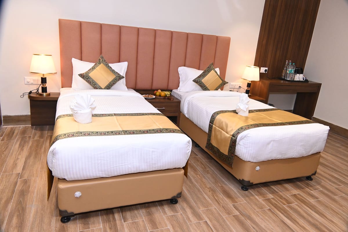 A hotel room with two beds, each with a brown suitcase, a wooden headboard, and a nightstand with a lamp.