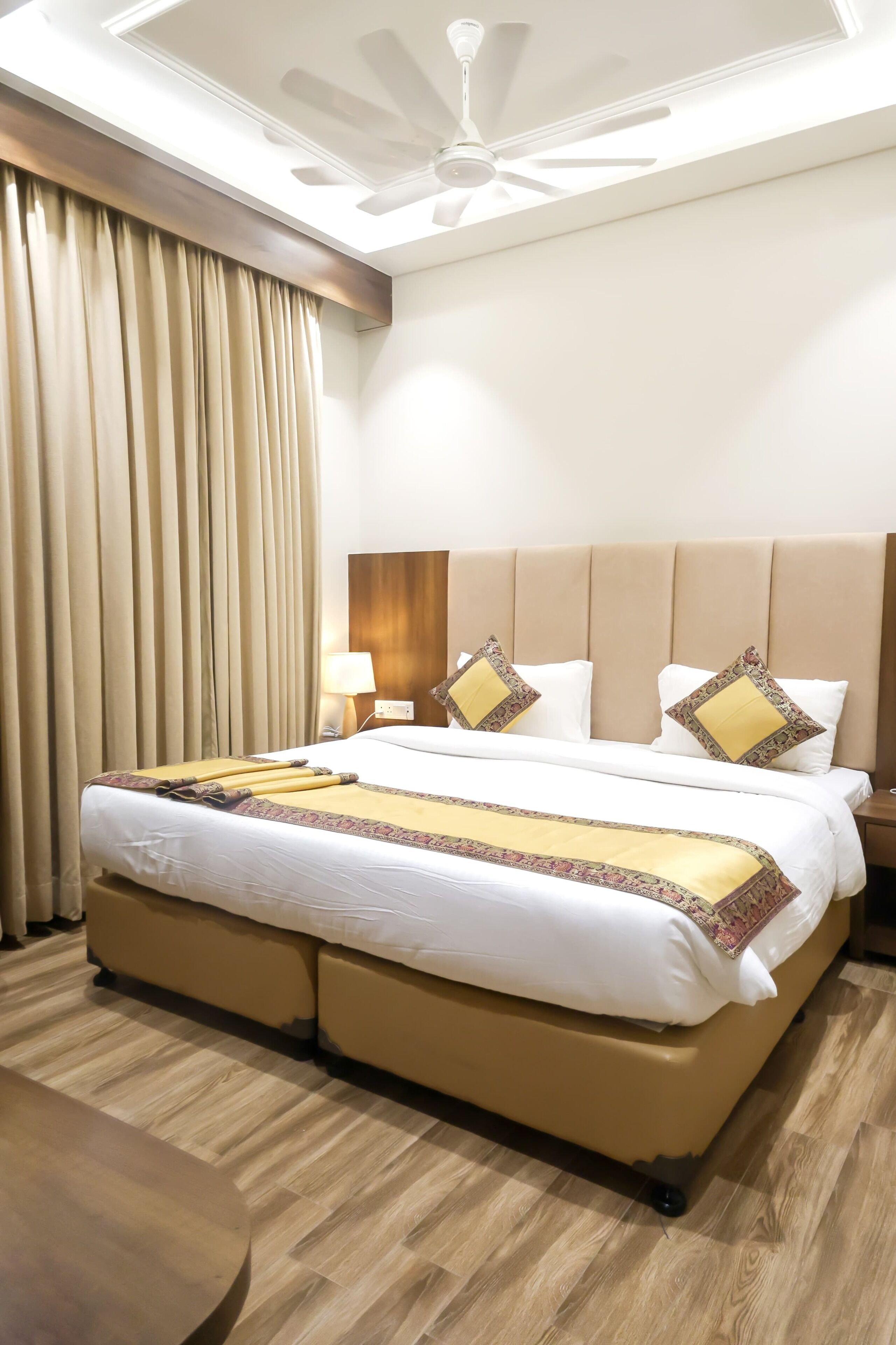 A hotel room with a large bed, a ceiling fan, and a wooden floor.