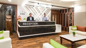 A reception area with a marble counter, two staff members, a wooden floor, and a modern interior design. - Hotel The Rising Banaras (Varanasi)
