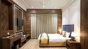 A hotel room with a bed, bedside table, lamp, and a TV on a wooden cabinet. - Hotel The Rising Banaras (Varanasi)