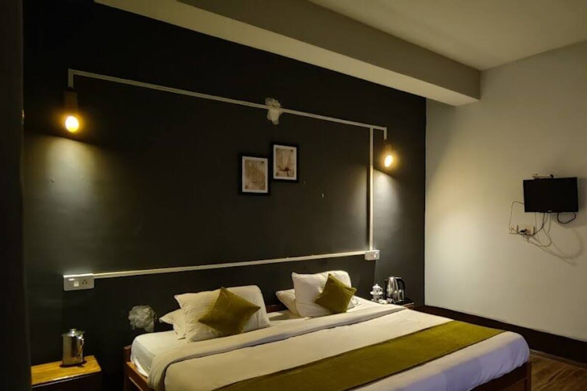 Een hotelkamer met een bed, nachtkastje, wandtelevisie en kunstwerk.