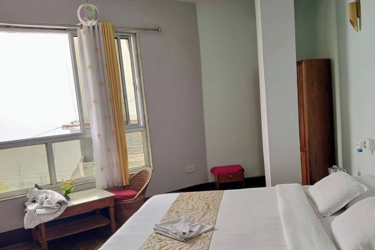Een hotelkamer met een bed, een raam met gordijnen, een stoel, een kleintje tafeltje en een schilderij aan de muur.