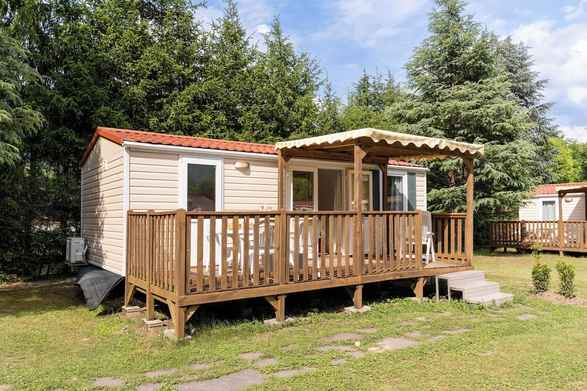 Een stacaravan met een houten terras, een overdekte veranda en een kleine aangelijmde garage.