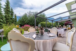 An outdoor dining area with round tables, chairs, and a view of mountains. - Club del Sole Due Laghi Levico (Levico Terme)