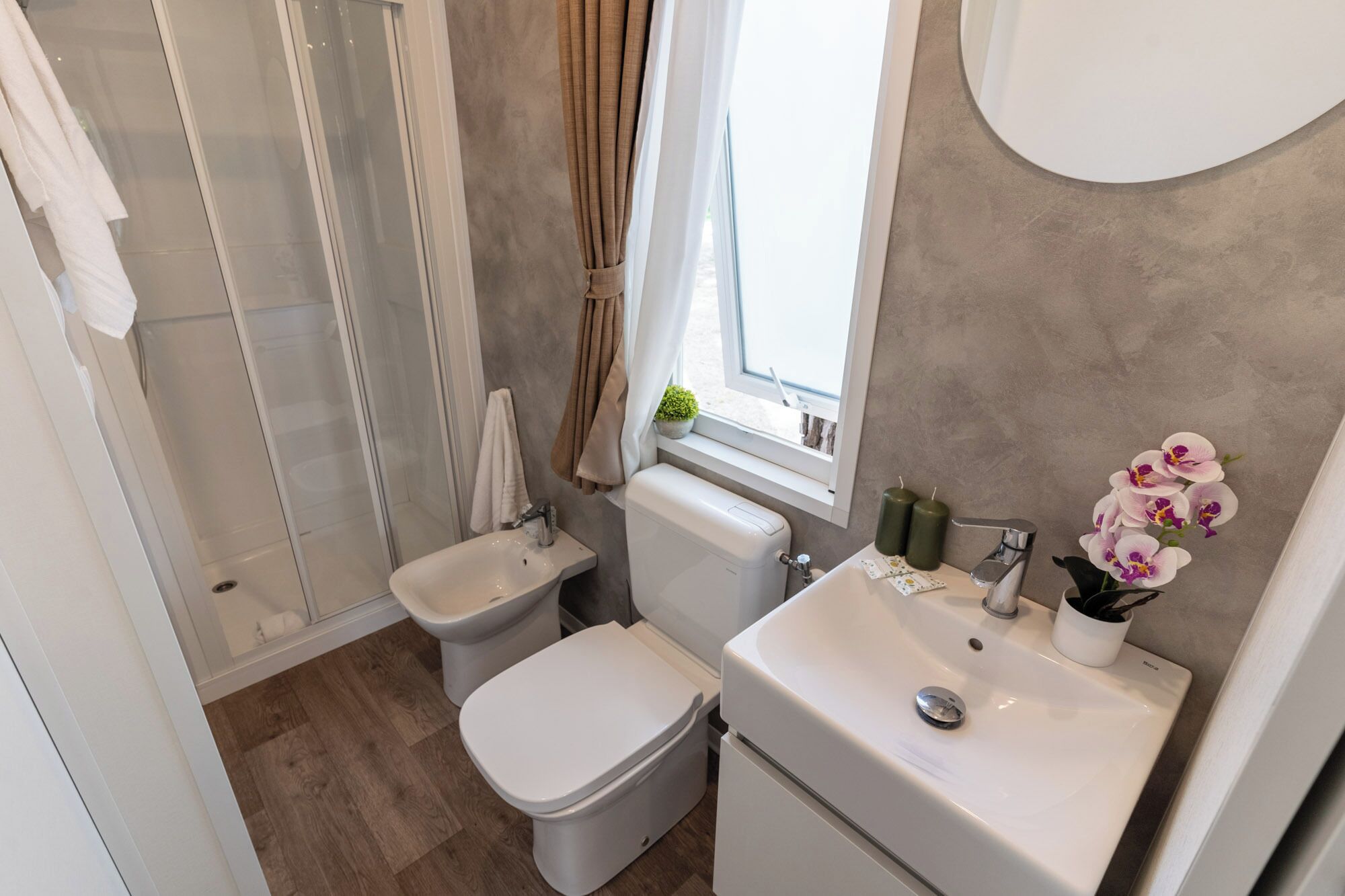 A bathroom with a shower, two toilets, a sink, and a window with curtains.