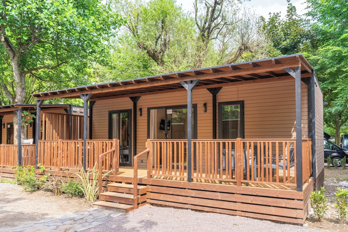 Een houten hut met een veranda, een deur waarop '5513' staat en een kleine trap naar de ingang.