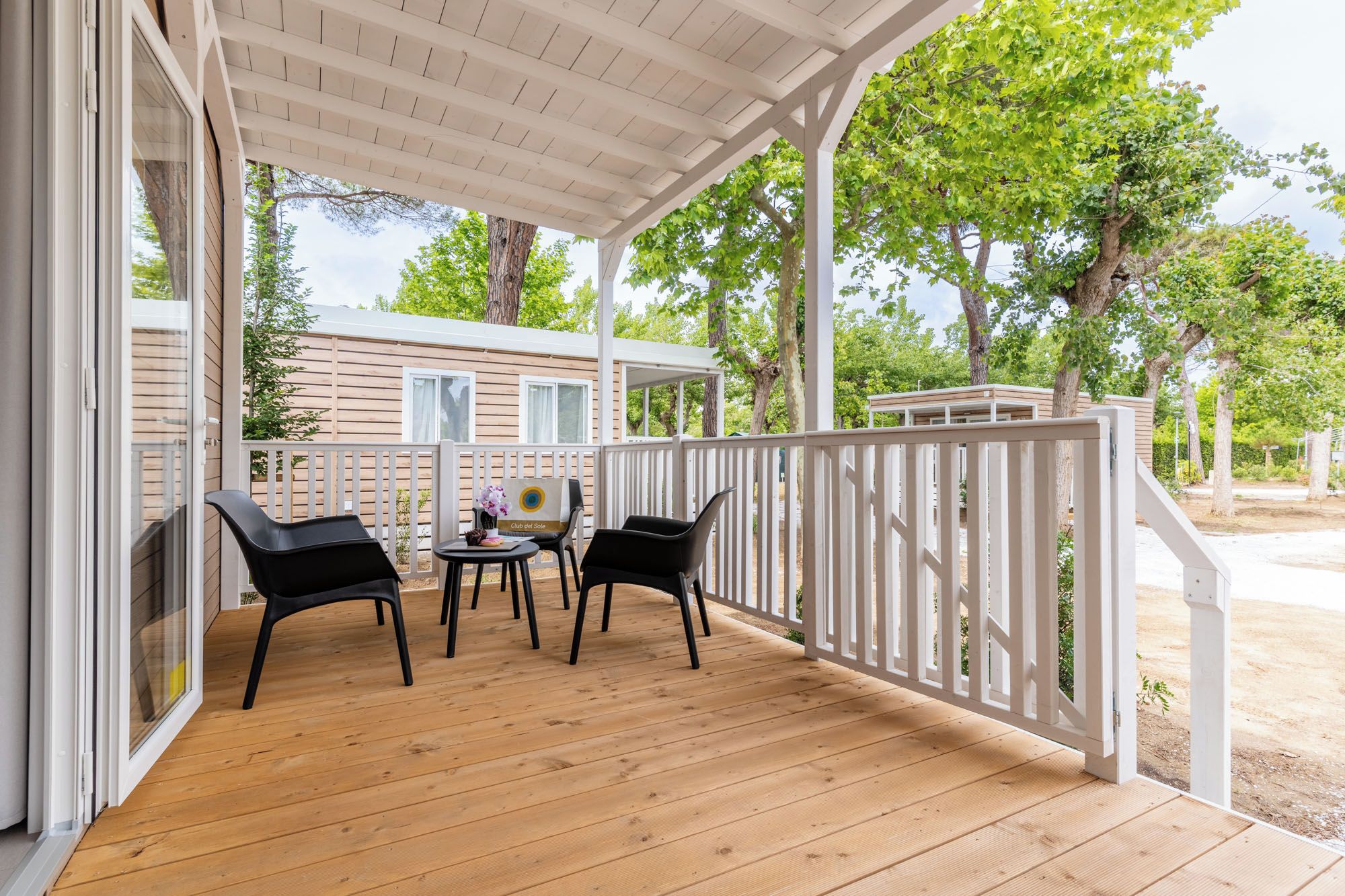 A covered outdoor area with a wooden deck, white railing, and two black chairs.
