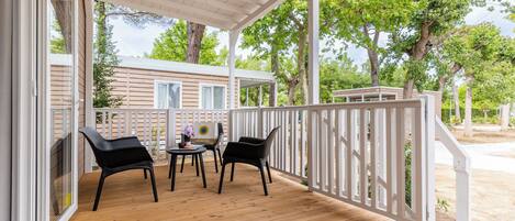 A covered outdoor area with a wooden deck, white railing, and two black chairs.