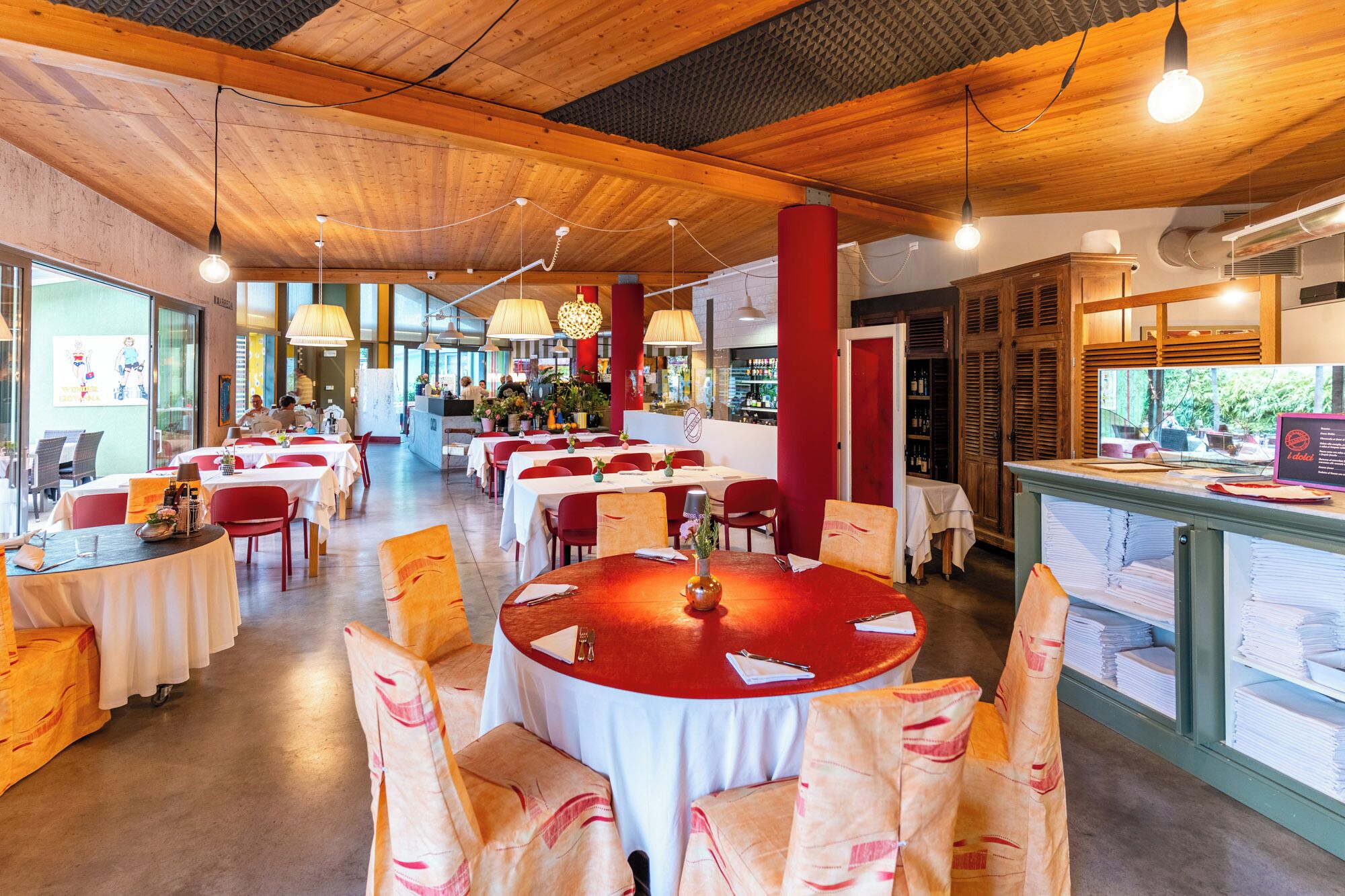 Ein Restaurant mit runden Tischen, roten Stühlen und einer Holzbalkendecke.