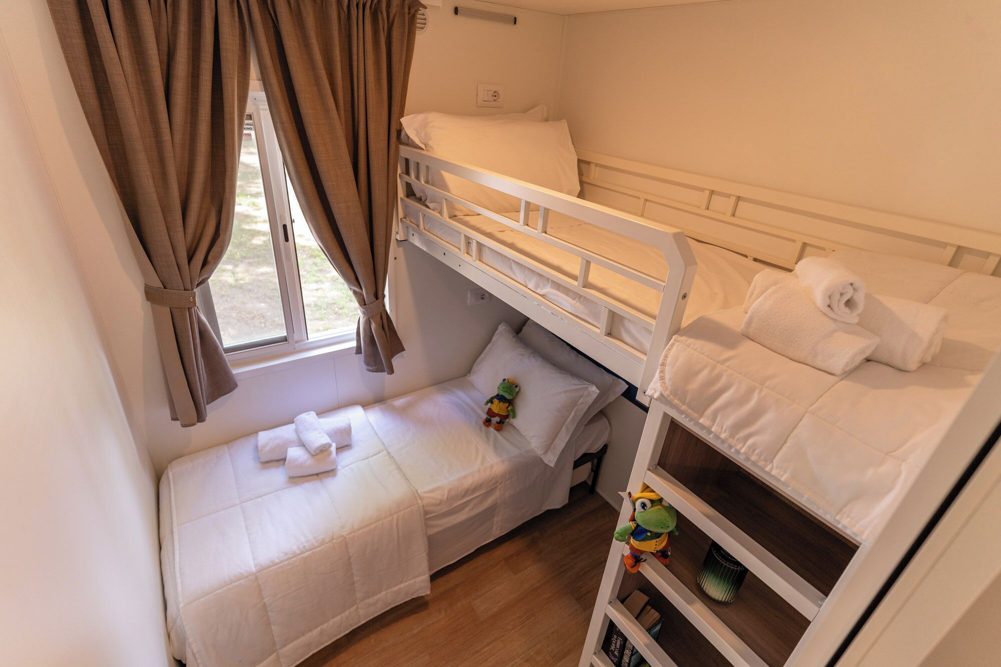 A bunk bed room with a window, curtains, and a small table with a toy.